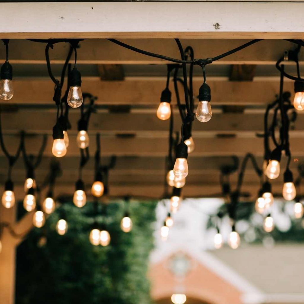 festoon lighting strings are hanging from a wooden pergola outside
