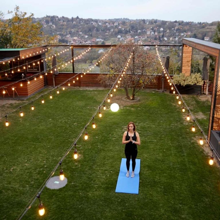 Festoon light strings hung in garden with a girl standing on a blue yoga mat in the middle